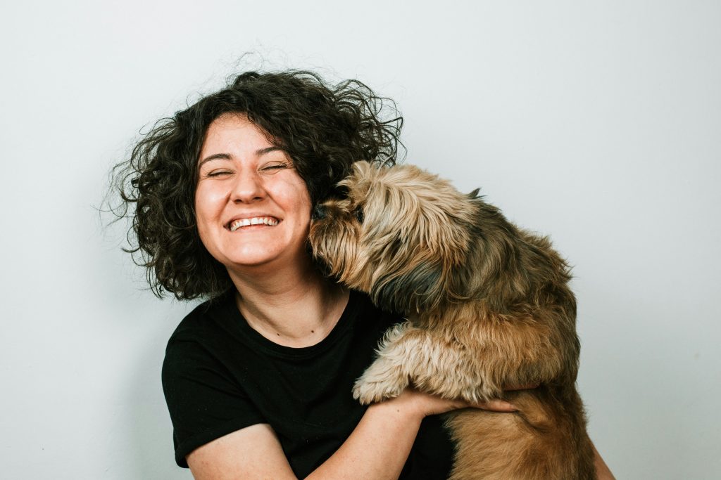 woman smiling holding dog sniffing or kissing her face